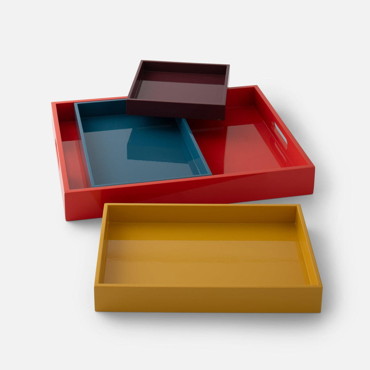 Angled view of Stacking Trays, Set of 4 showcasing four nesting lacquer trays in red, blue, burgundy, and butterscotch on a white background