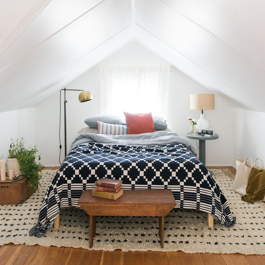 Bed topped with a navy geometric coverlet and layered pillows in a bright attic bedroom with sloped white ceiling