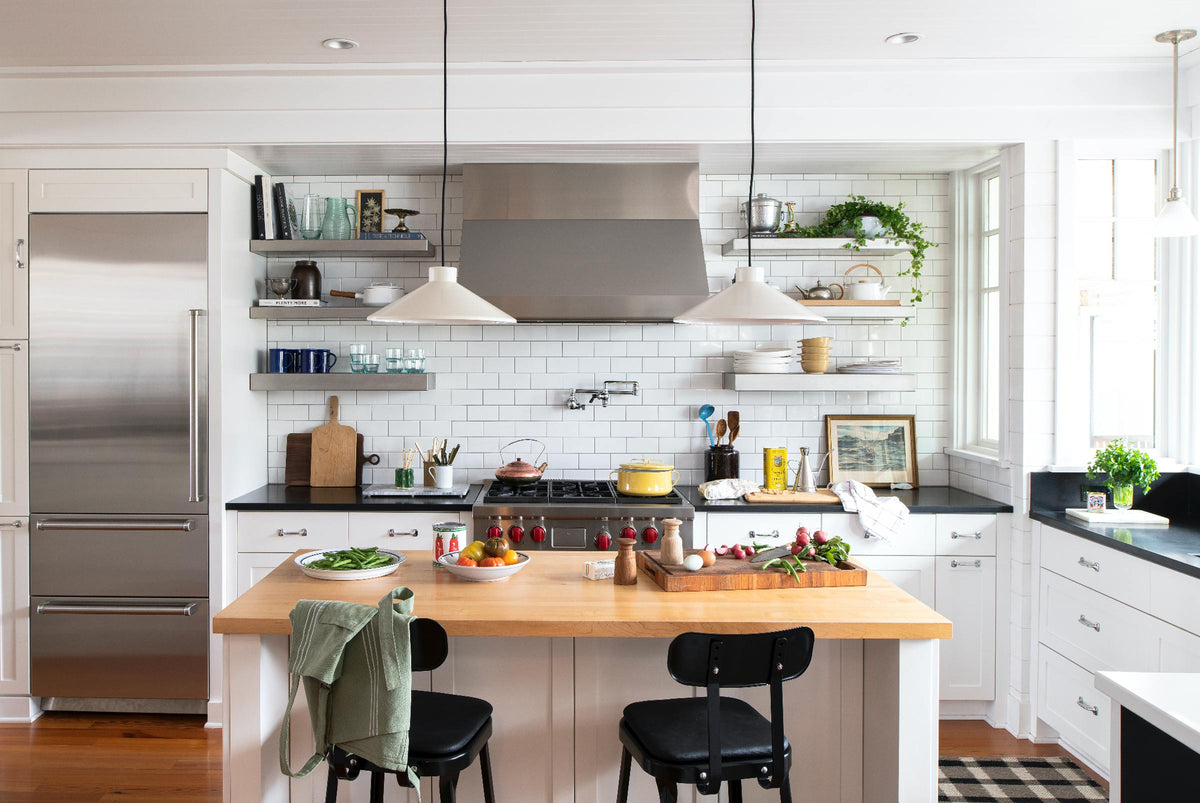 Two white pendant lights over a wood-top island with subway-tile backsplash and stainless refrigerator