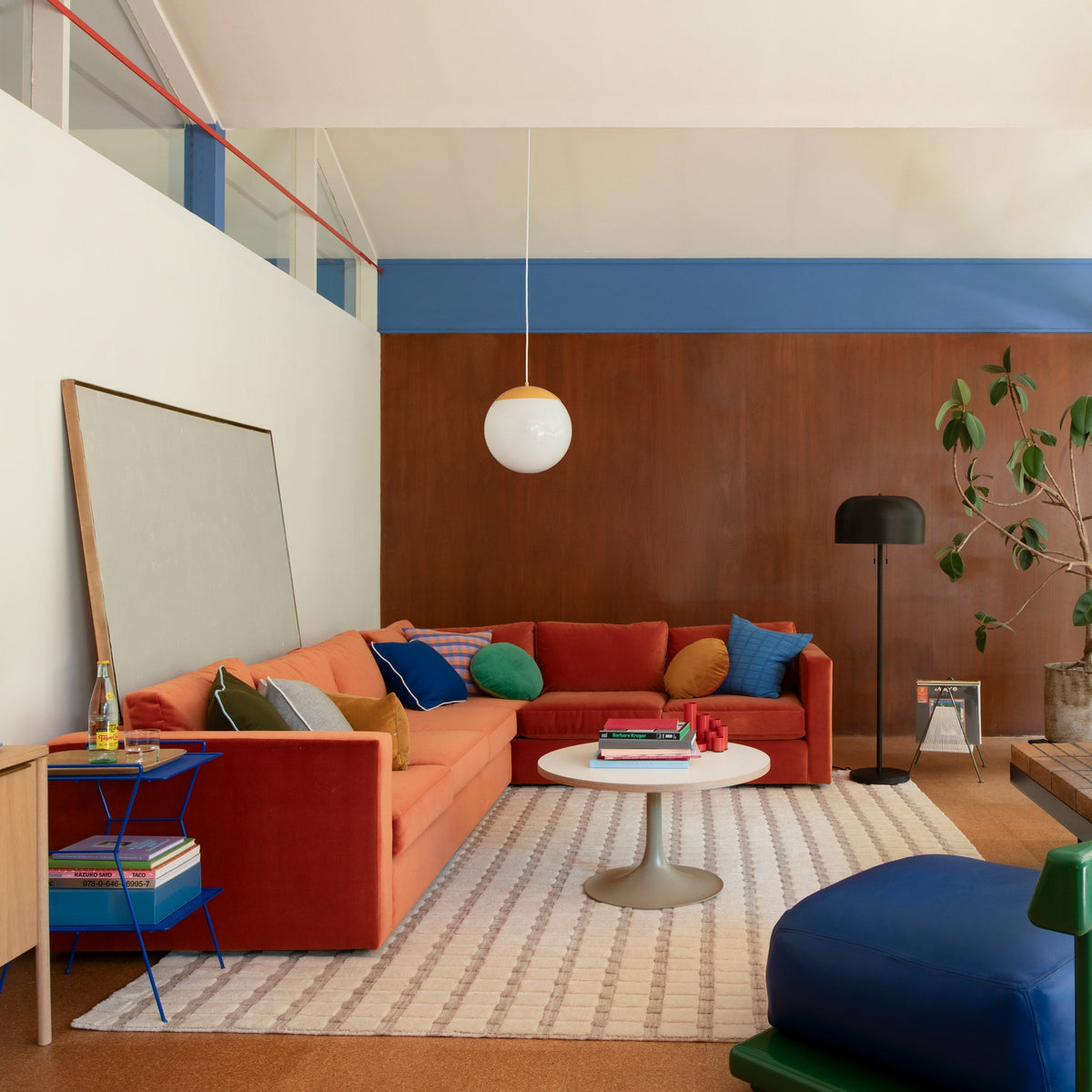 Mid-century living room with orange sectional sofa, colorful pillows, round pendant light, wood-paneled wall and coffee table