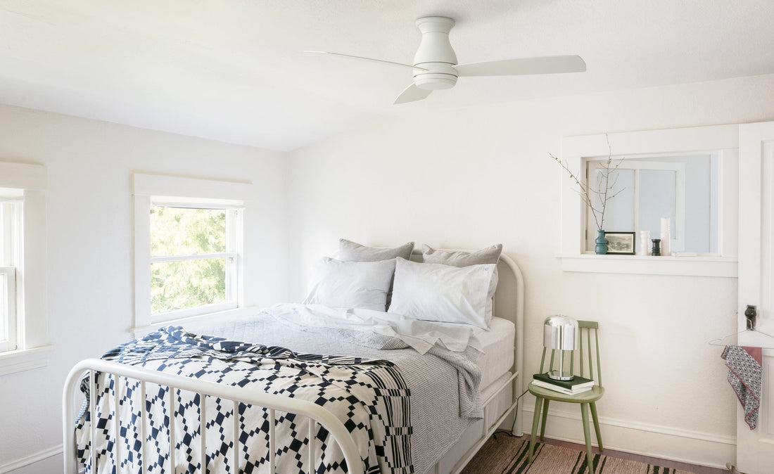 White ceiling fan above a bright bedroom with a metal bed, gray pillows, navy-and-white patterned blanket and green chair