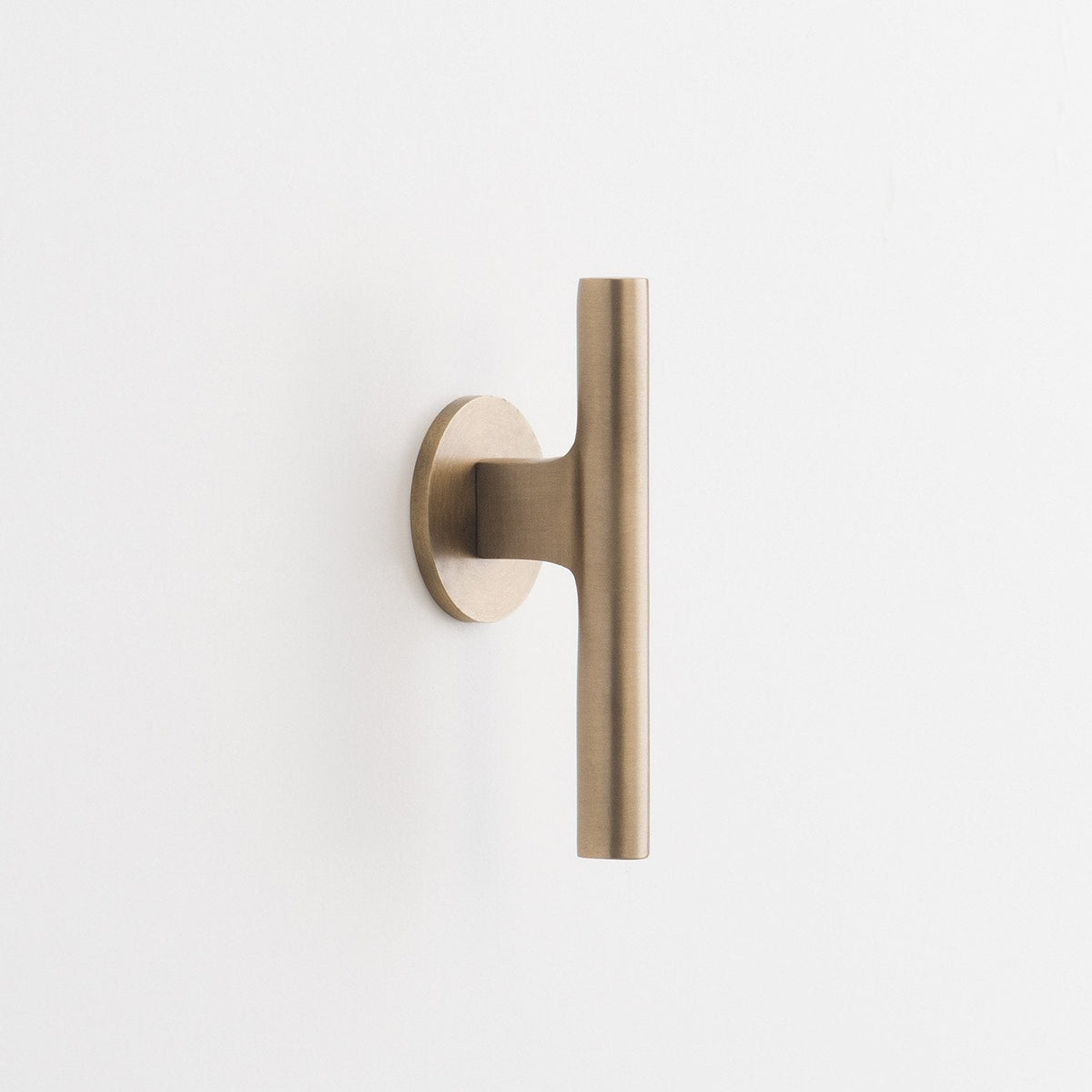 Front view of the natural brass Galley Pull showcasing its asymmetrical curved design and round backplate on a white background