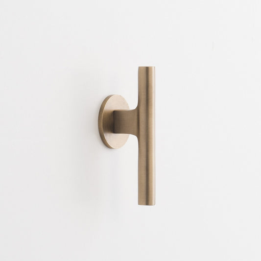 Front view of the natural brass Galley Pull showcasing its asymmetrical curved design and round backplate on a white background