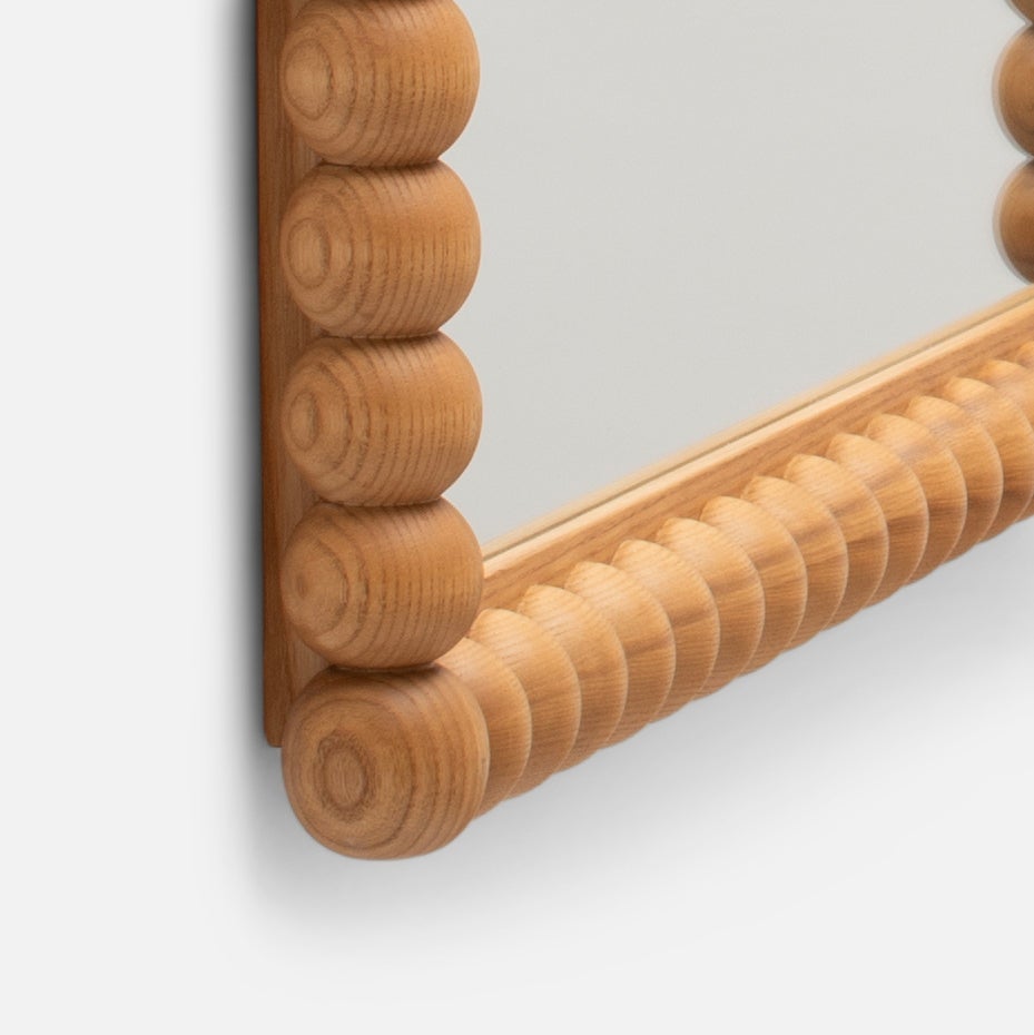 Close-up corner of Bobbin Mirror showing turned bobbin ash wood frame with visible wood grain on light gray background