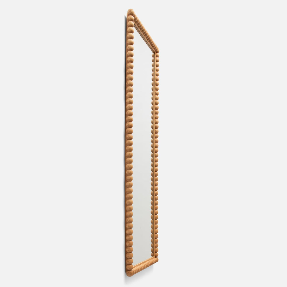 Three-quarter side view of Bobbin Mirror showcasing turned-wood bobbin frame in ash finish against a light background