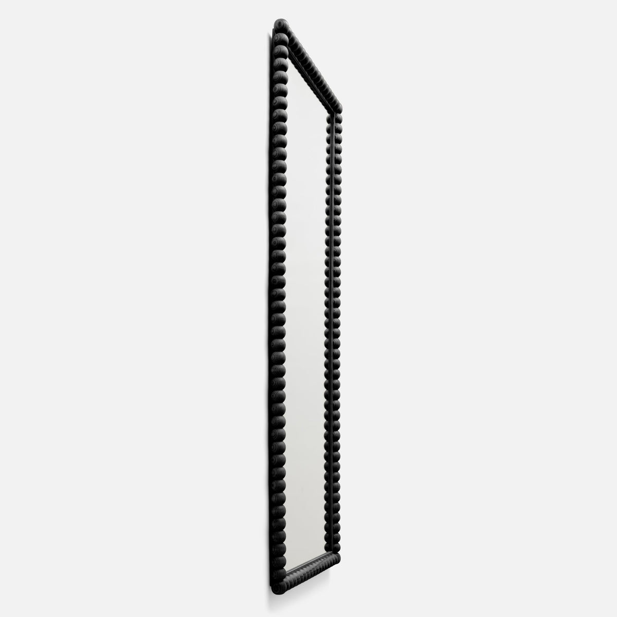 Angled side view of Bobbin Mirror, 28 x 68 in, showing black beaded wood frame and full-length mirror on white background