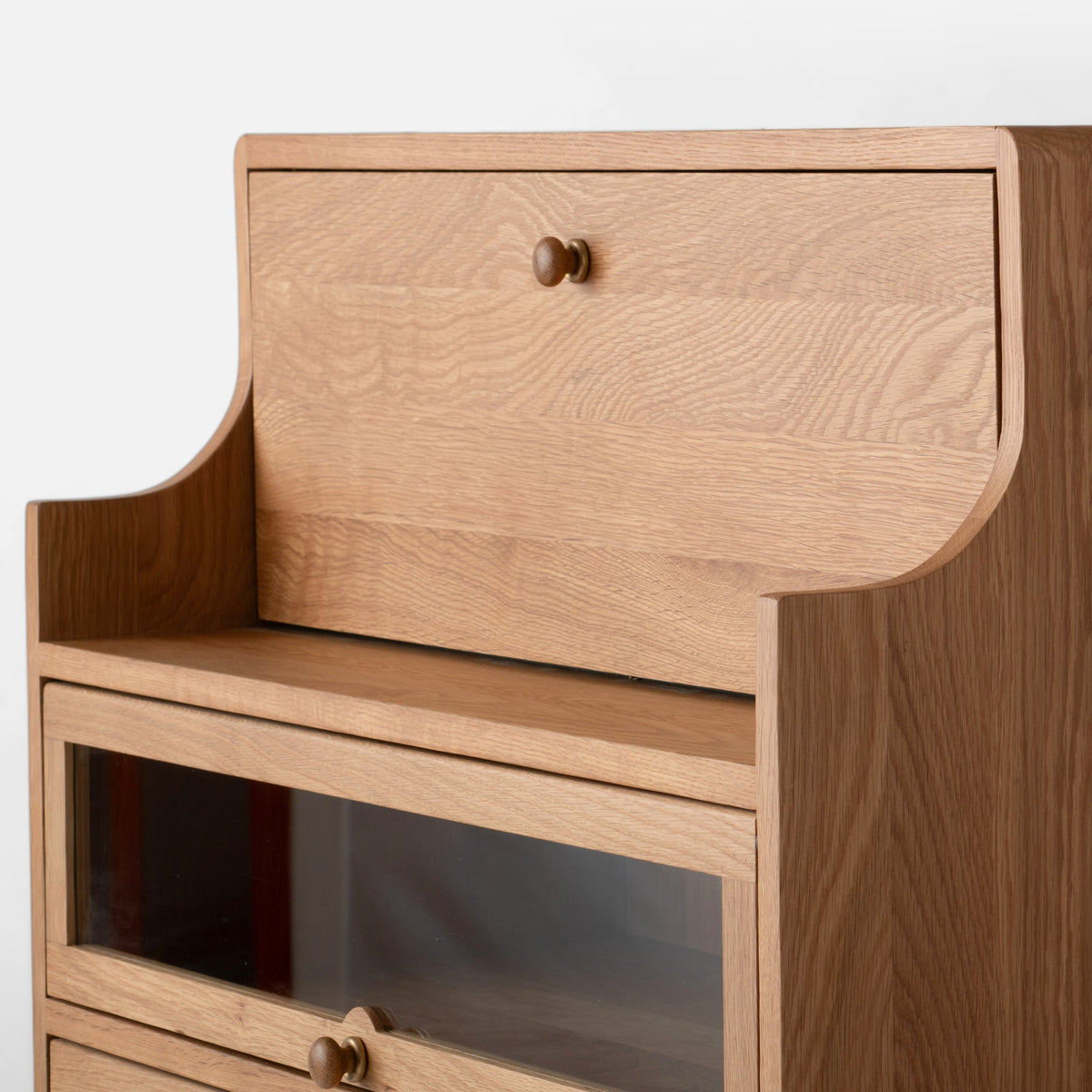 Close-up front-right view of Peggy Cabinet showcasing wood grain, rounded edges, and a glass-front compartment against a white background