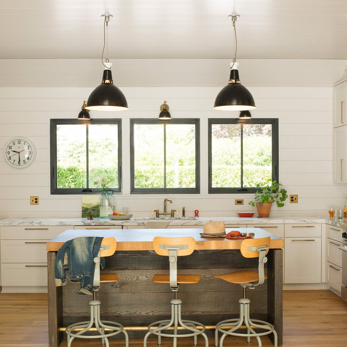 Bright kitchen showcasing brass Edgecliff pulls on white cabinets, with marble countertops, a wood island, and three black pendant lights