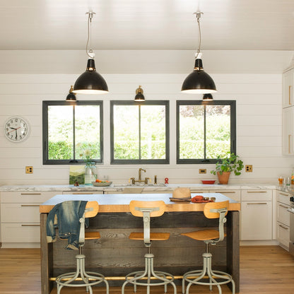 Bright kitchen showcasing brass Edgecliff pulls on white cabinets, with marble countertops, a wood island, and three black pendant lights