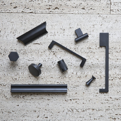Top-down view of Edgecliff Appliance Pull alongside black cabinet hardware on a textured light stone surface