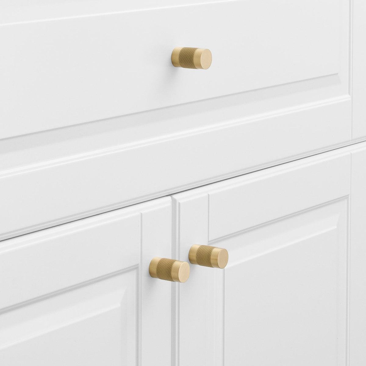 Three natural brass knurled knobs installed on white paneled cabinet doors