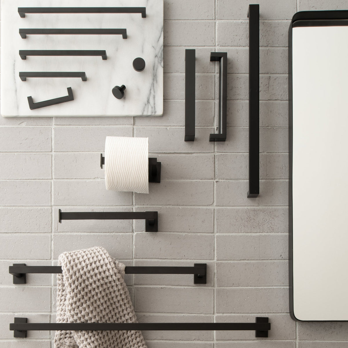 Black Edgecliff bathroom hardware displayed on a light gray tiled wall with a mirror and towels
