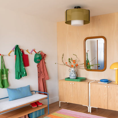 Tula hooks hold coats and hats on a colorful wall in a warm entryway with a bench and wood cabinets
