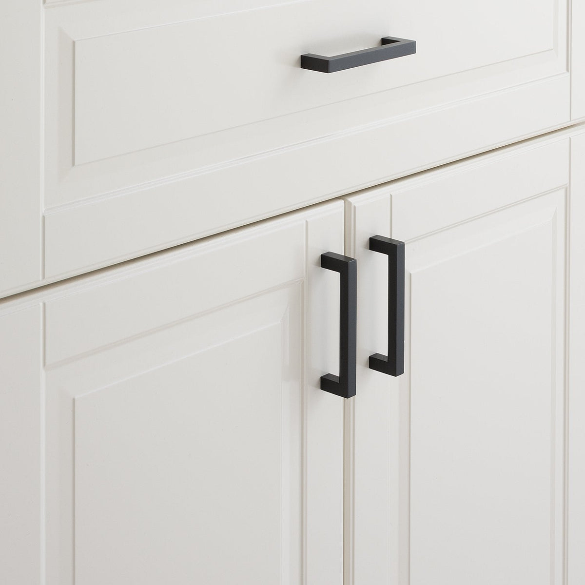 Close view of Edgecliff Pull showcasing its black bar design with white paneled cabinets