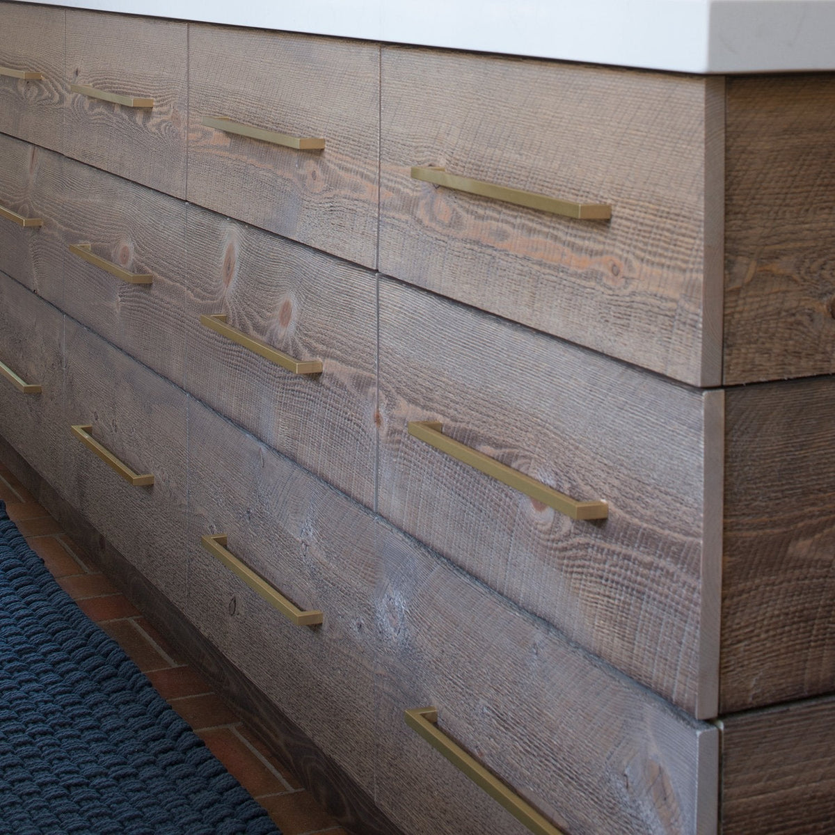 Multiple Edgecliff appliance pulls installed on textured wood drawers beside a dark blue rug