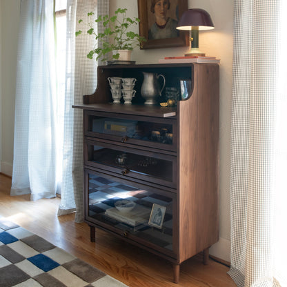 Three quarter view of Peggy Cabinet showcasing curved sides and glass front storage drawers in a sunlit room