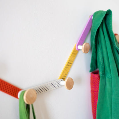Angled view of the multicolor Tula Hook showcasing perforated metal and wood finials on a white wall