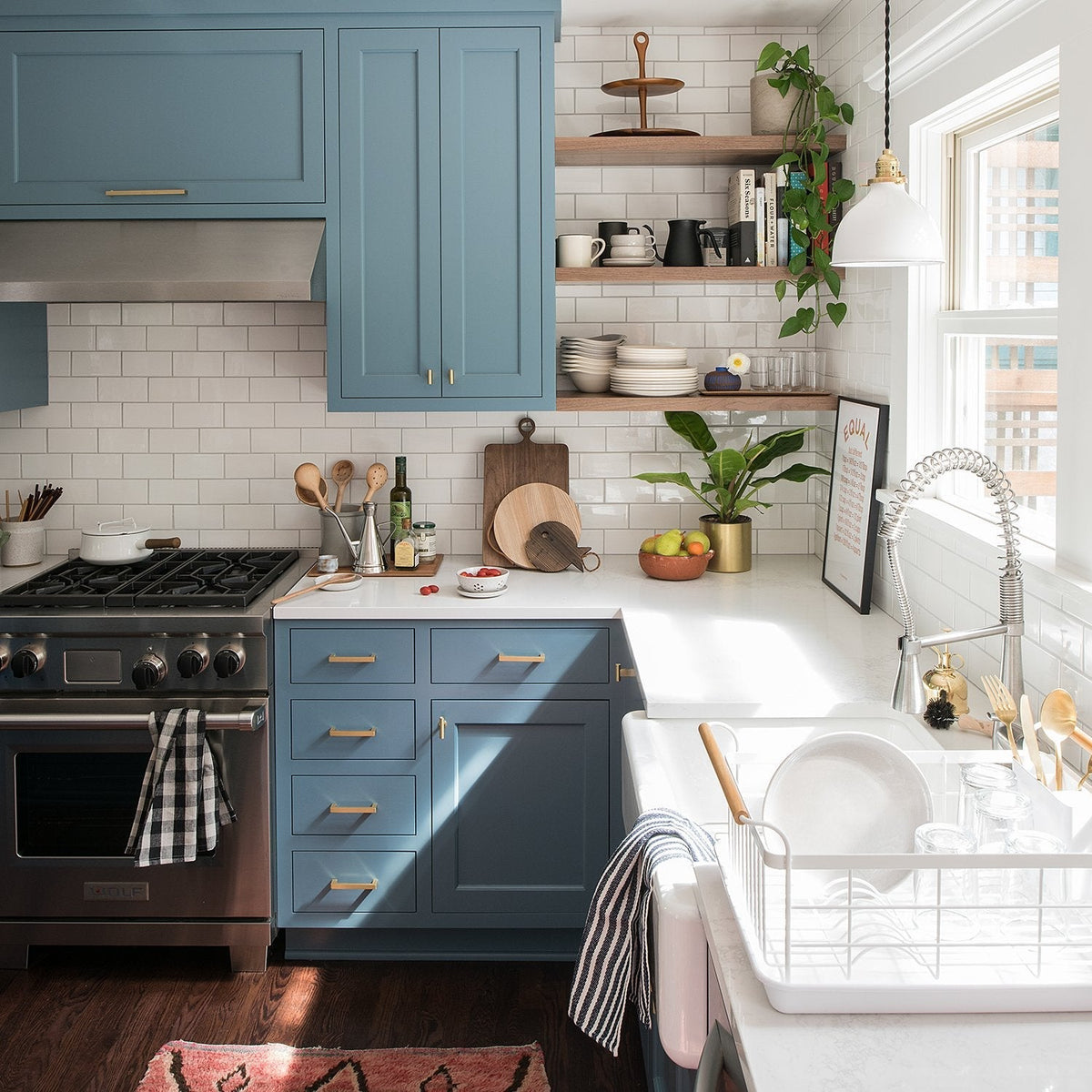 Blue kitchen cabinets with Edgecliff appliance pulls beside a bright farmhouse sink