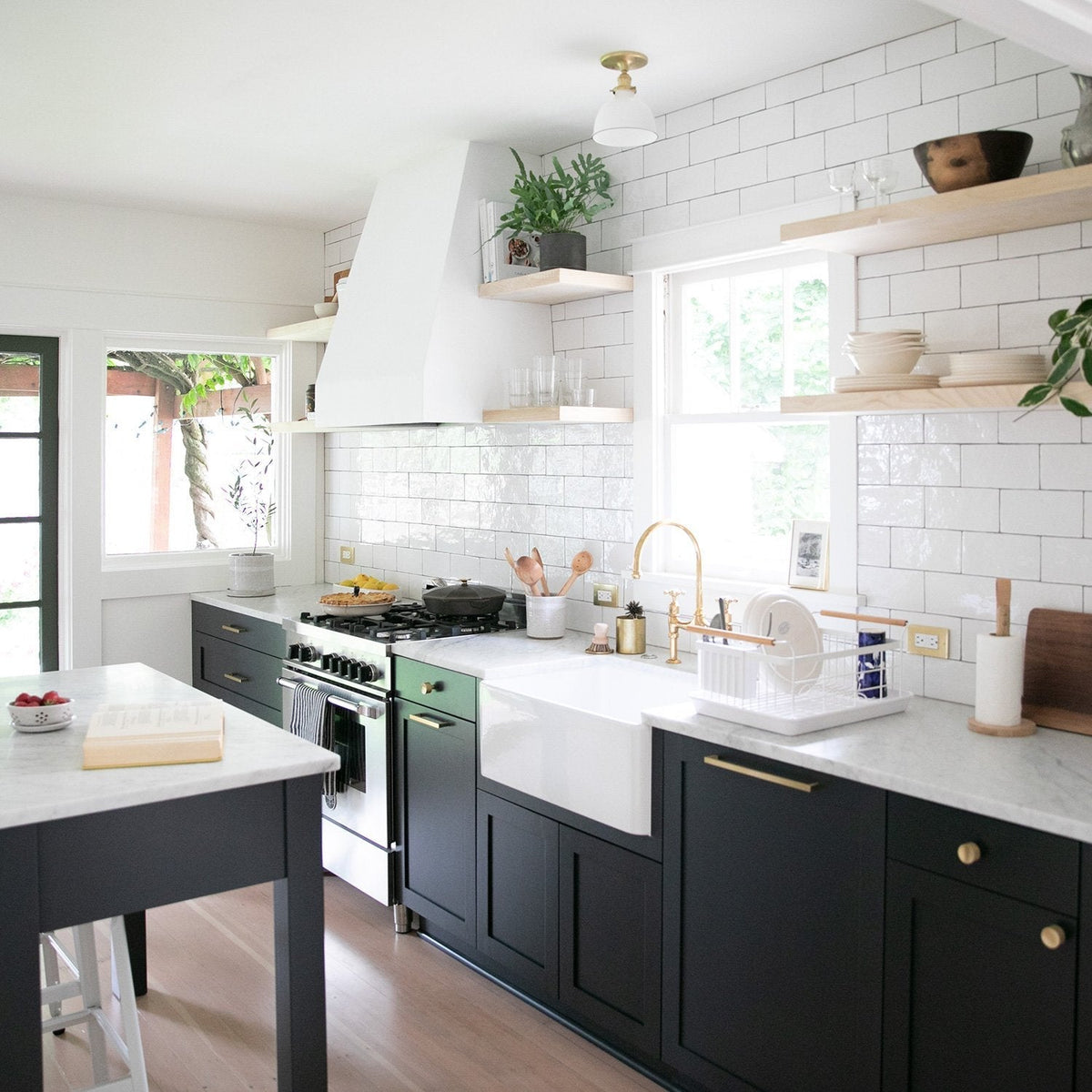 Bright kitchen featuring Edgecliff appliance pulls on dark cabinetry, white tile backsplash, open shelves, and a farmhouse sink