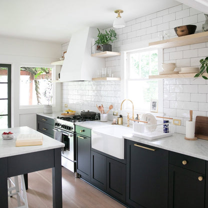 Bright kitchen featuring Edgecliff appliance pulls on dark cabinetry, white tile backsplash, open shelves, and a farmhouse sink