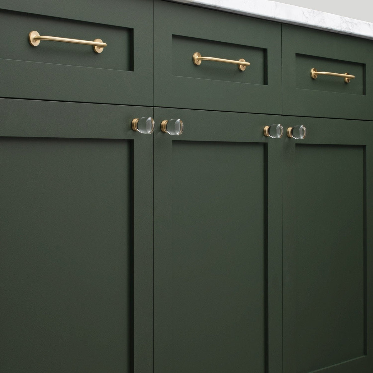 Close-up view of Parker Pull showcasing slim gold-tone bar pulls with round mounts on dark green cabinetry