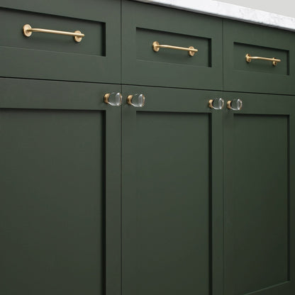 Close-up view of Parker Pull showcasing slim gold-tone bar pulls with round mounts on dark green cabinetry