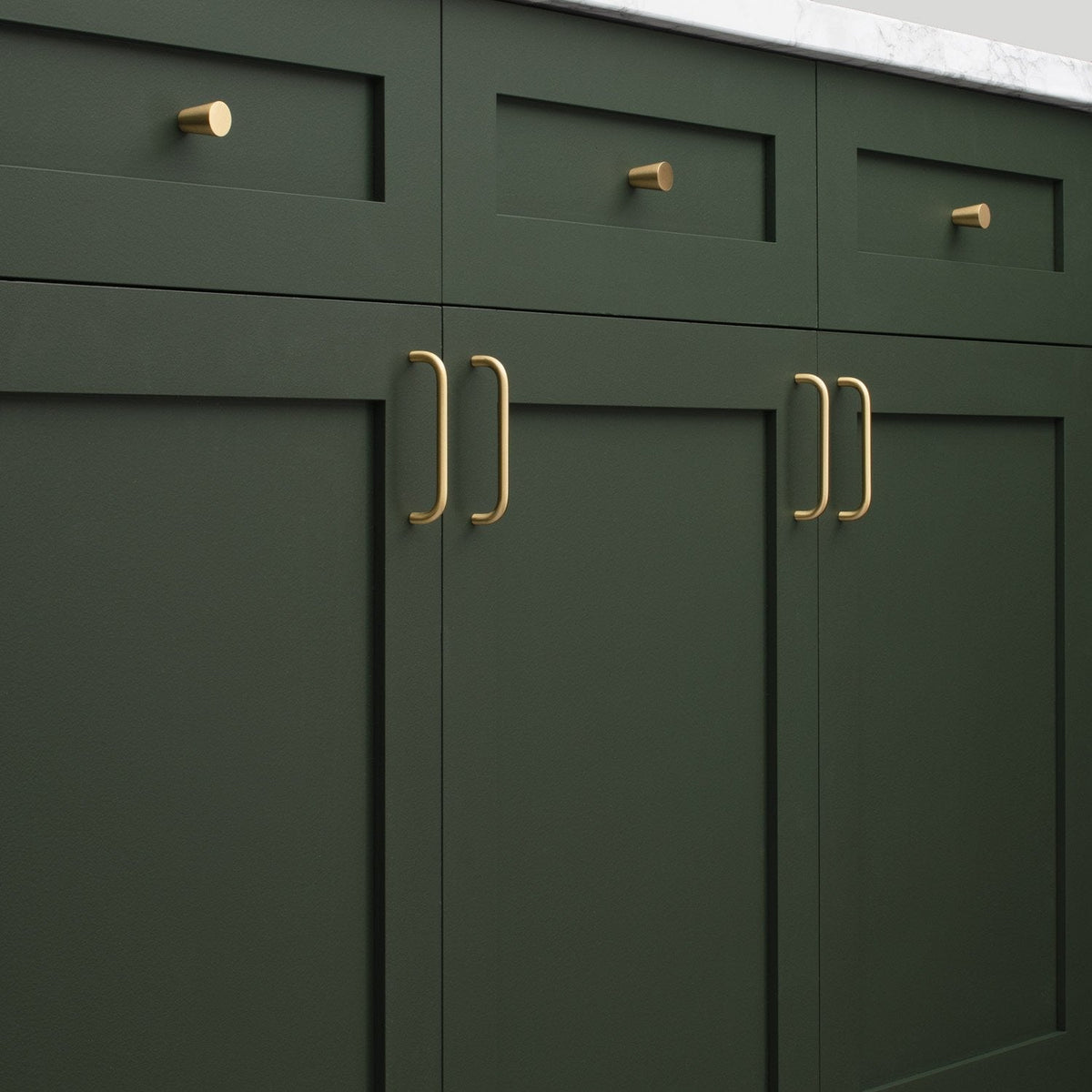 Close-up of Parker Pull hardware installed on dark green cabinetry, showing vertical bar pulls and matching round knobs
