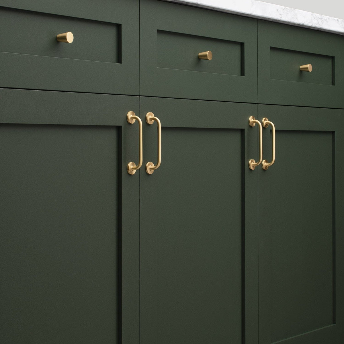 Close-up view of Parker Pull cabinet handles showcasing a gold-tone finish on dark green cabinetry