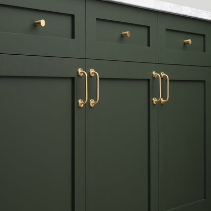 Close-up view of Parker Pull cabinet handles showcasing a gold-tone finish on dark green cabinetry