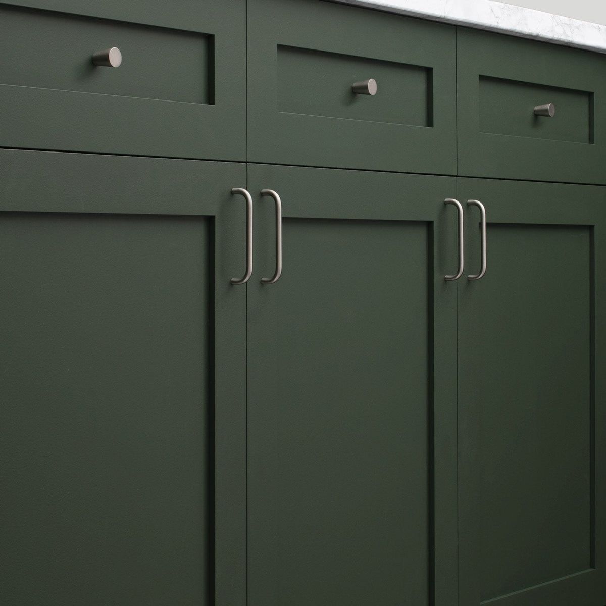Close-up of Parker Pull showcasing curved handles installed on dark green paneled cabinets